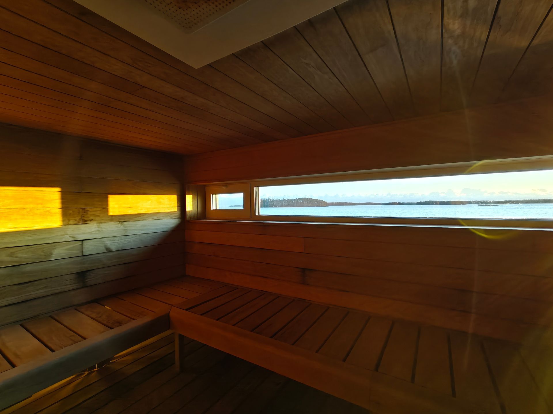 Puupaneloitu saunan sisustus, jossa on porrastetut penkit ja vaakasuora ikkuna, josta on näkymä vesistölle.