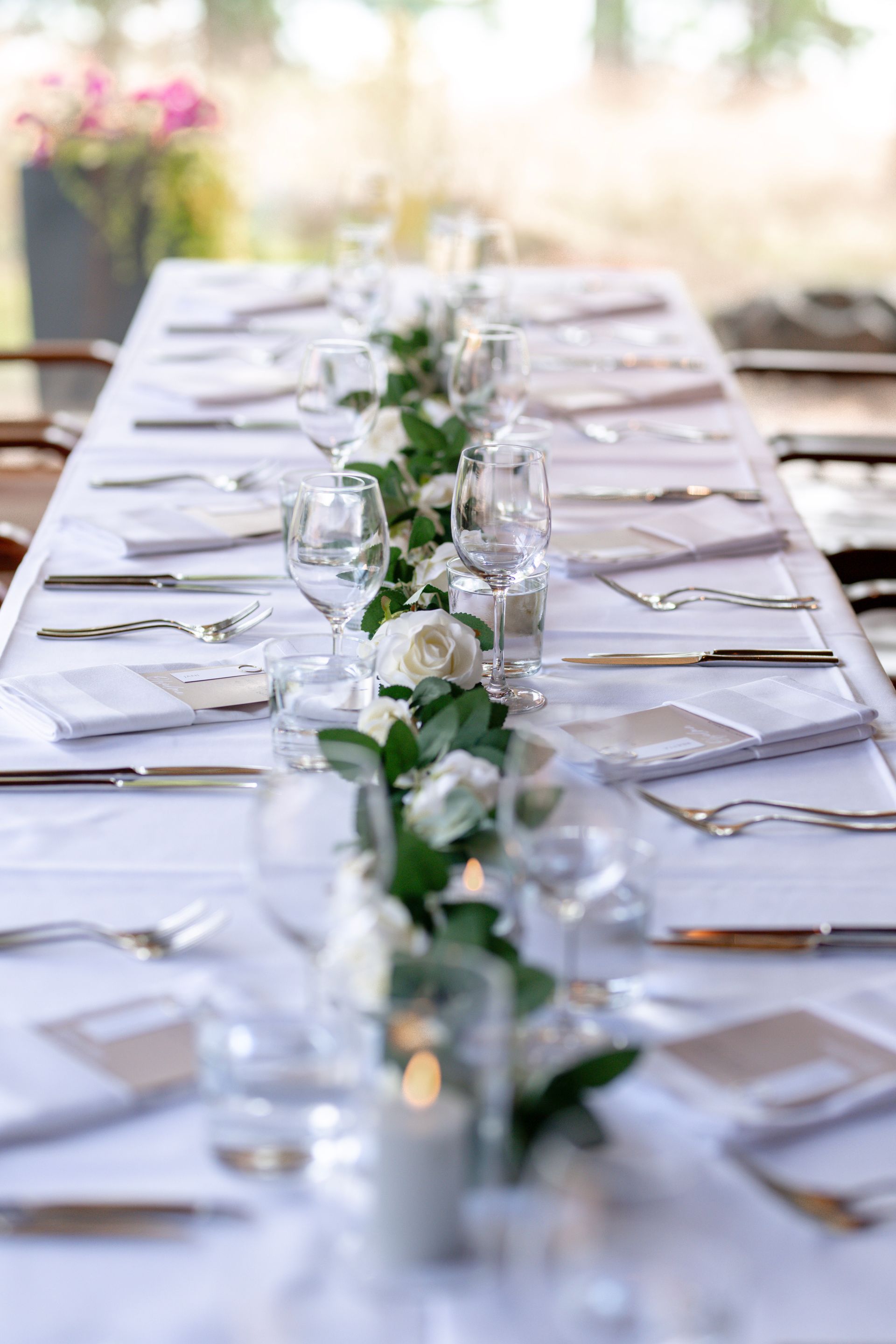 Pitkä pöytä katettu muodolliseen tilaisuuteen, johon kuuluu valkoiset liinavaatteet, aterimet, kristallilasit ja keskellä kukkakuvioinen eukalyptus-jalkapöytä.