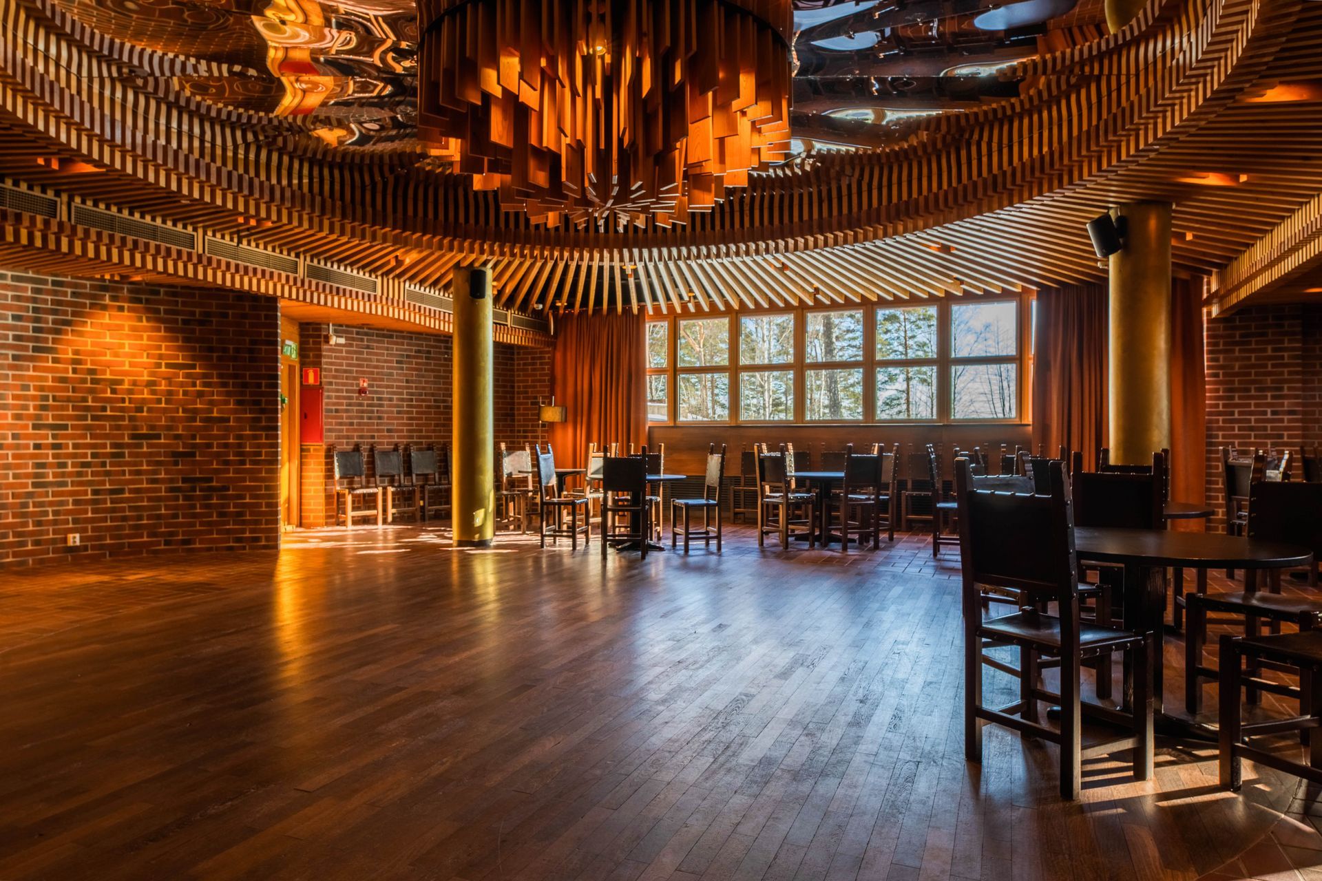 Tyylikäs, himmeästi valaistu ravintolasisustus, jossa on puulattia, tiiliseinät, suuri moderni kattokruunu ja tummat istuimet.