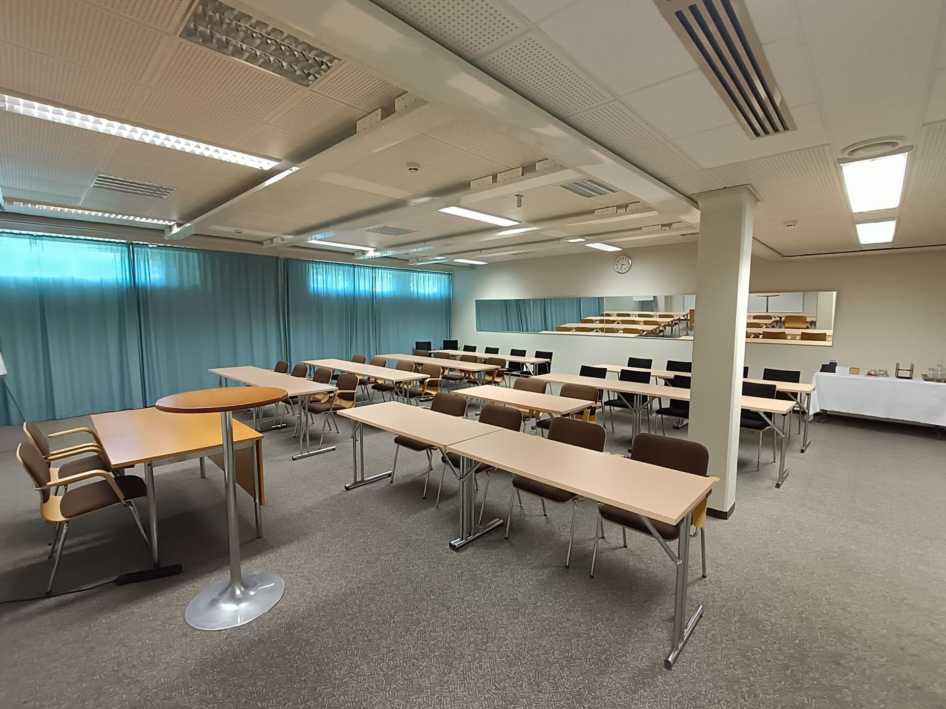 Tyhjä kokoushuone, jossa on rivi pöytiä ja tuoleja, vaaleat puukalusteet ja sinivihreät verhot.