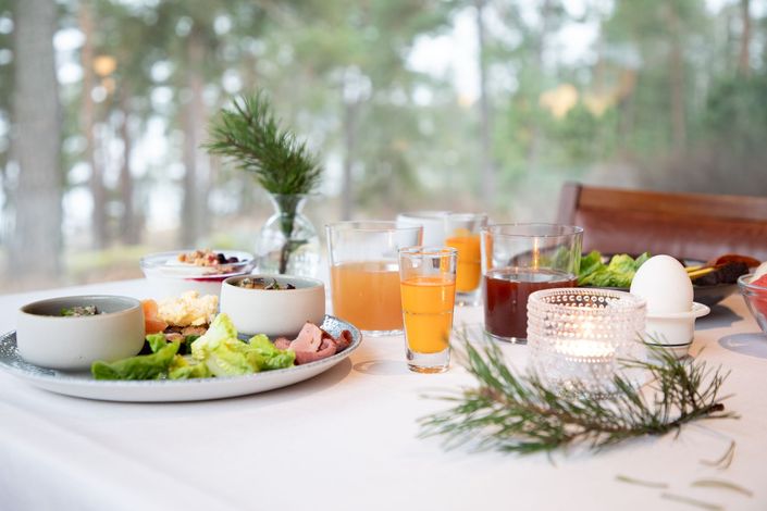 Aamiainen katettu pienillä kulhoilla ruokaa, laseilla mehua ja kynttilällä valkoisella pöydällä ikkunan lähellä.