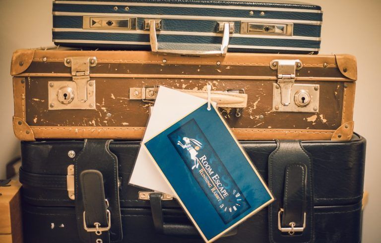 Kolmen vintage-matkalaukun pino, josta keskimmäisen kahvasta roikkuu sinivihreä 