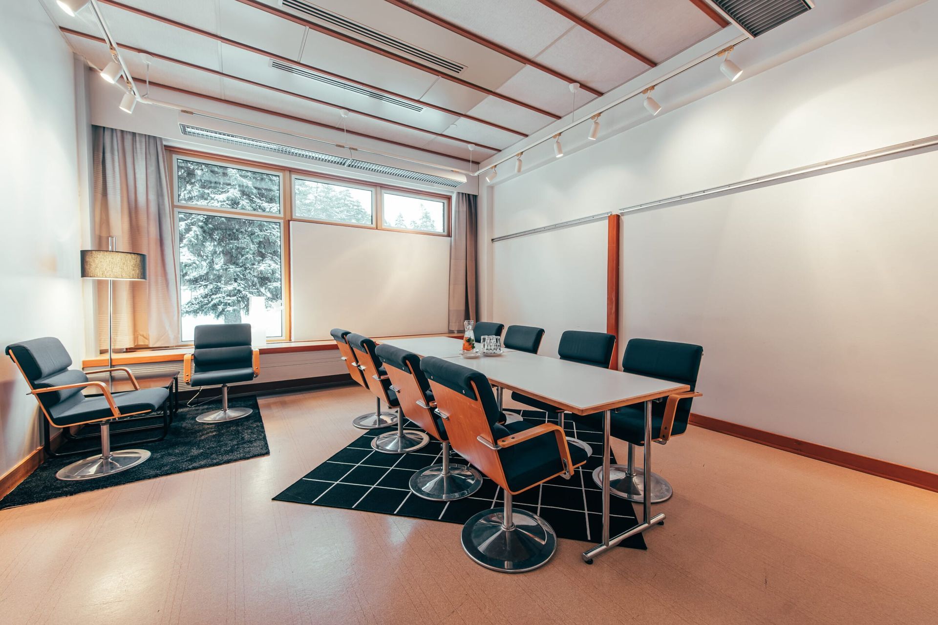 Moderni, valoisa kokoushuone, jossa on pitkä pöytä tuoleineen, sivuistuinryhmä ja suuret ikkunat.