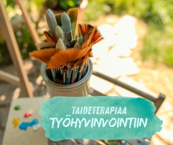 A container of paintbrushes with a watercolor-style overlay reading "TAIDETERAPIAA TYÖHYVINVOINTIIN" above a paint palette.