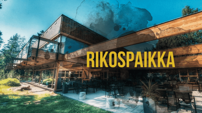 Moderni puurakennus, jossa on suuri ulkoterassi kirkkaan sinisen taivaan alla ja teksti "RIKOSPAIKKA".