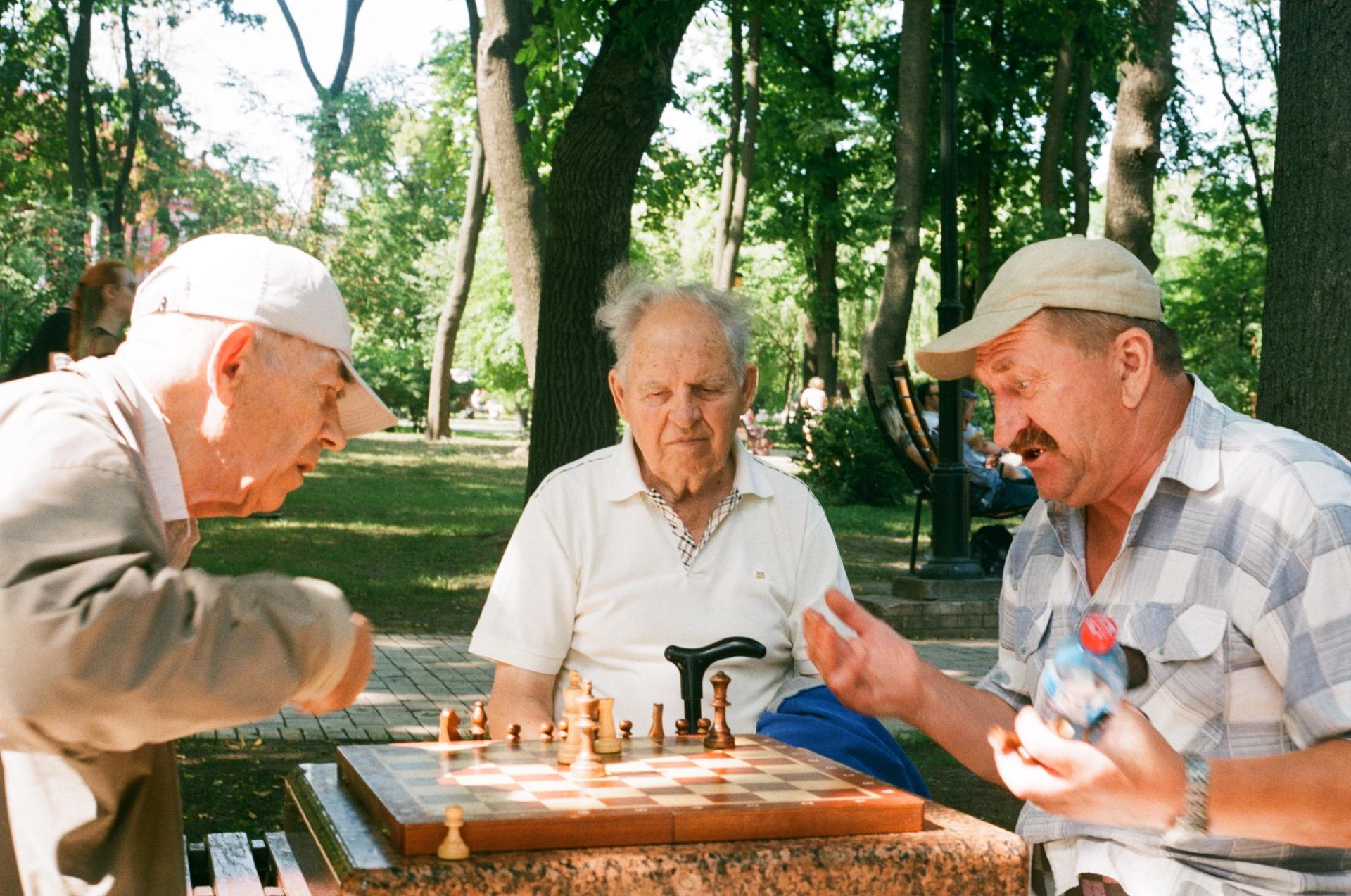 Three older men are playing chess in a park