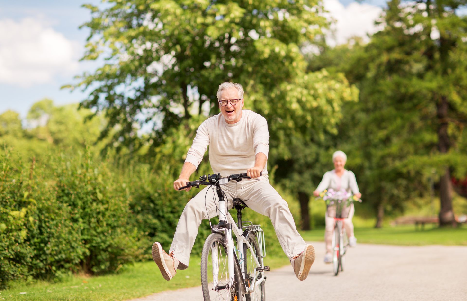 An elderly couple is riding bicycles down a path in a park.