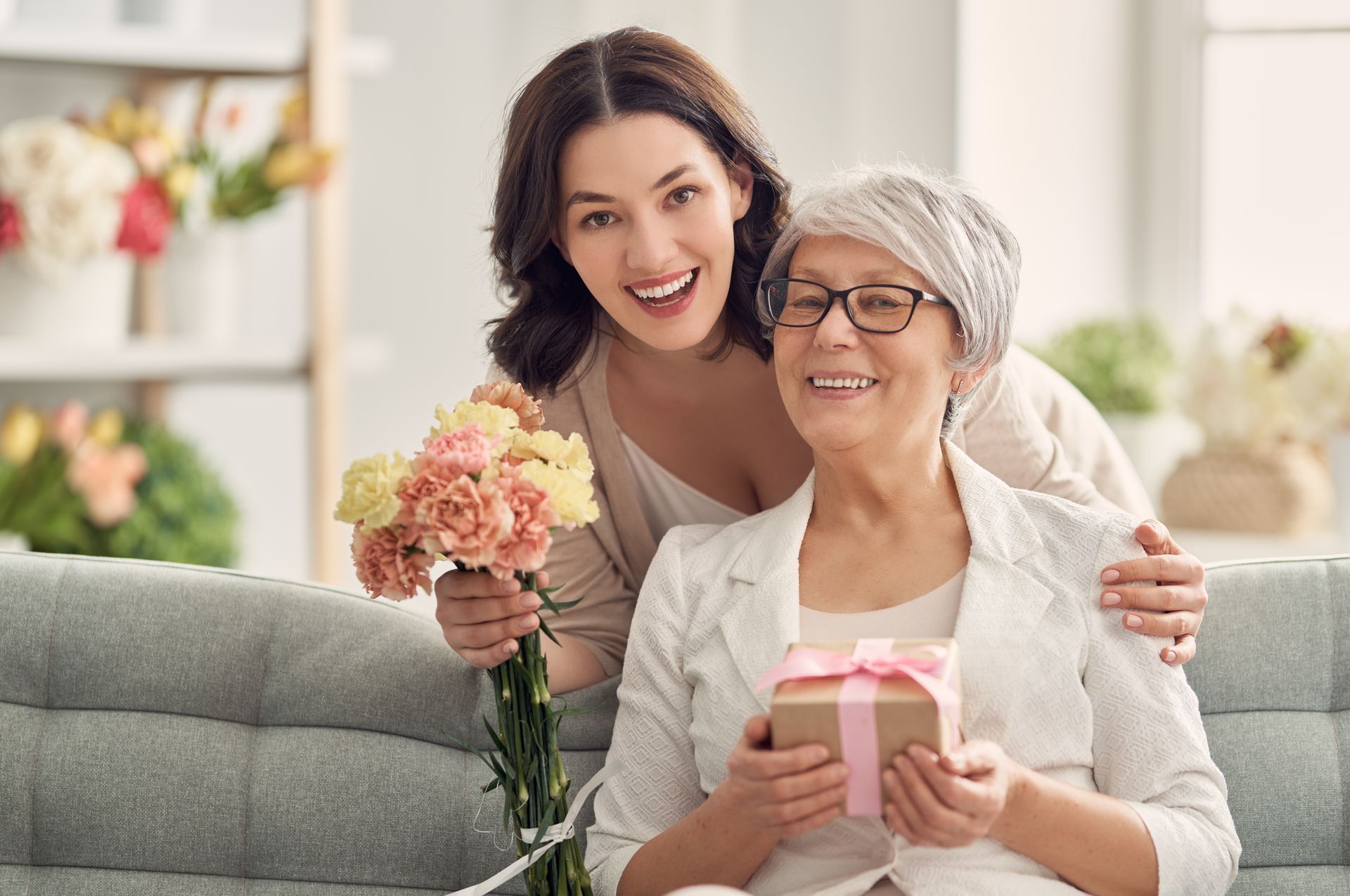 A young woman is giving an older woman a gift and flowers.