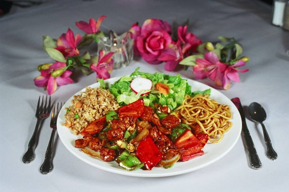 Plate of Asian food: General Tso's chicken, fried rice, noodles, and salad. Surrounded by flowers and silverware.