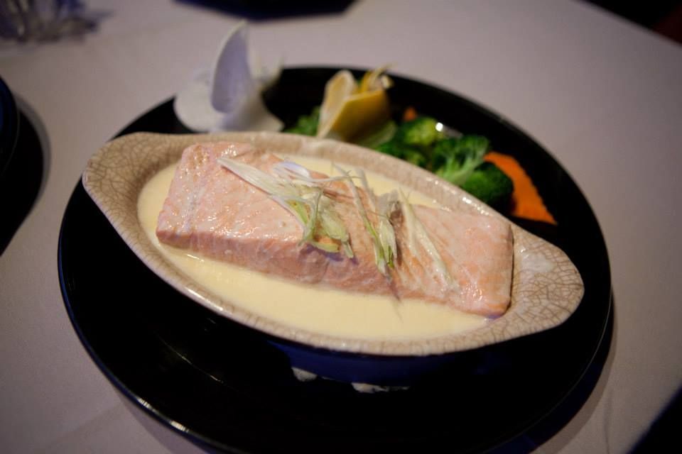 Salmon fillet in creamy sauce, served with vegetables on a black plate.