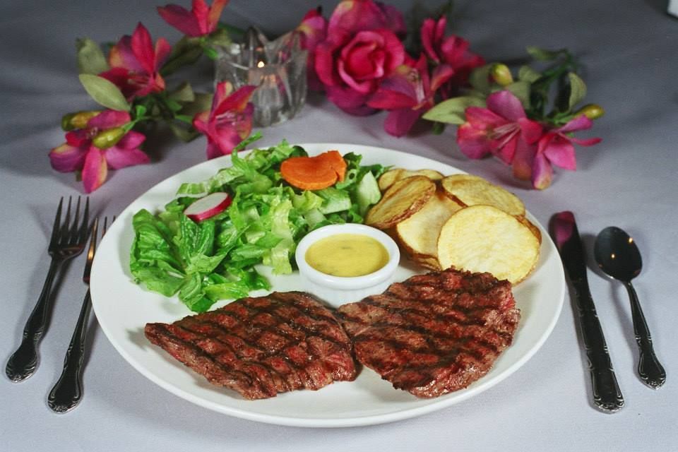 Grilled steak dinner with salad, potatoes, and dipping sauce, served on a white plate with silverware.