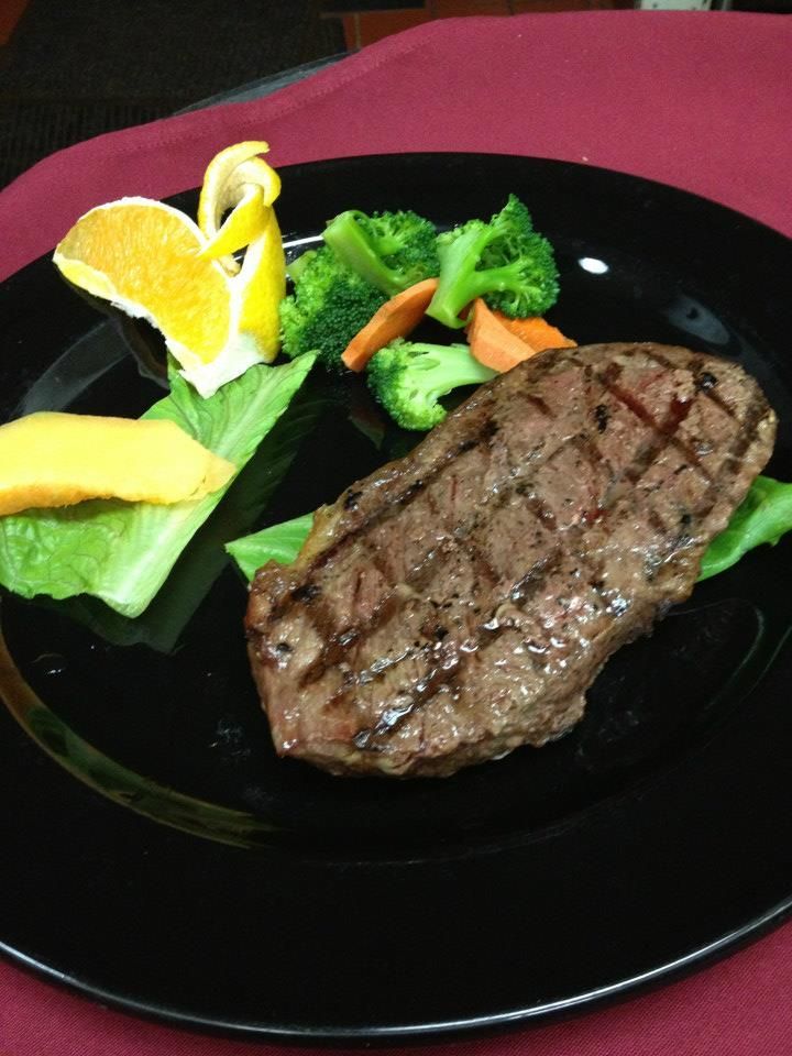 Grilled steak with vegetables and citrus garnish on a black plate.