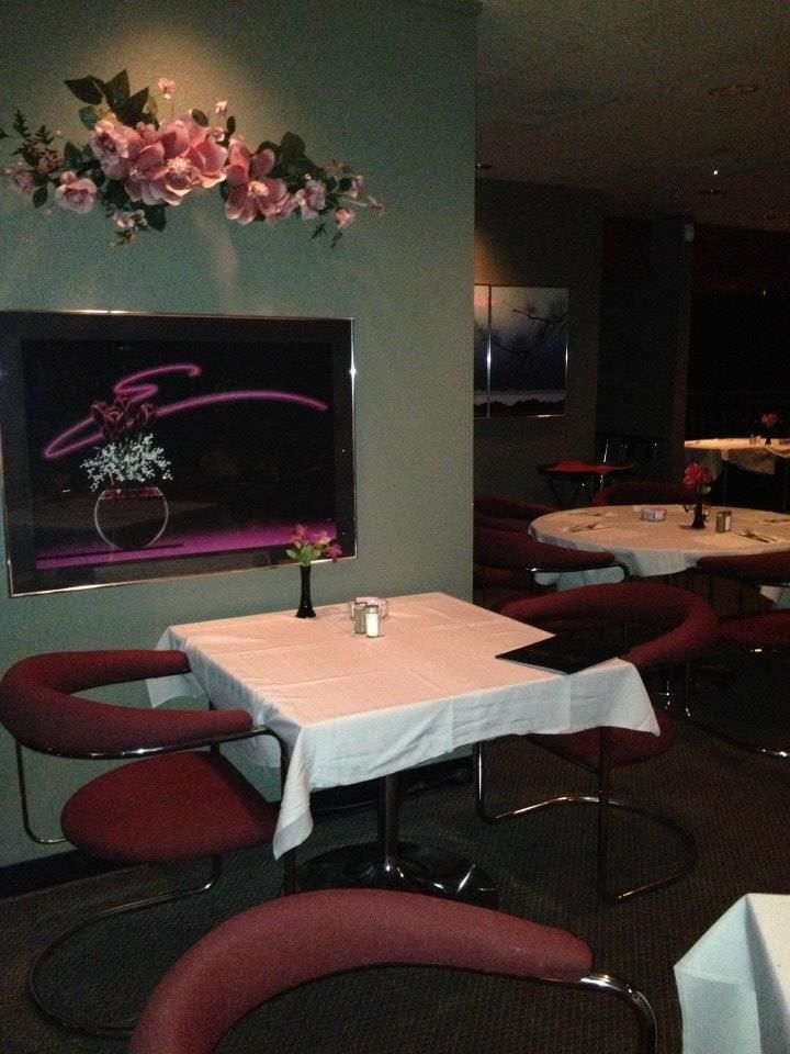 Restaurant dining area: square table set with white cloth, red chairs. Artwork and floral arrangement on the wall.