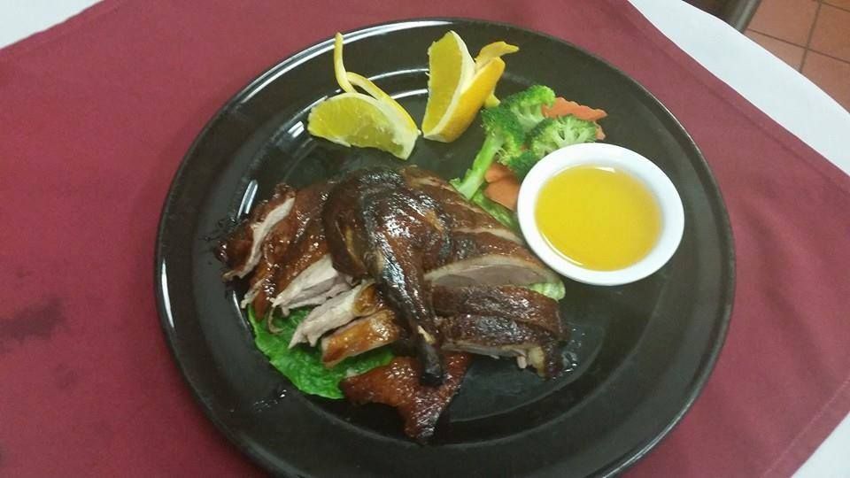 Roasted duck with sauce, vegetables, and citrus on a black plate, set on a red tablecloth.
