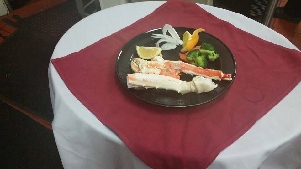A plate of crab legs, lemon wedge, vegetables on a round table with a red napkin.