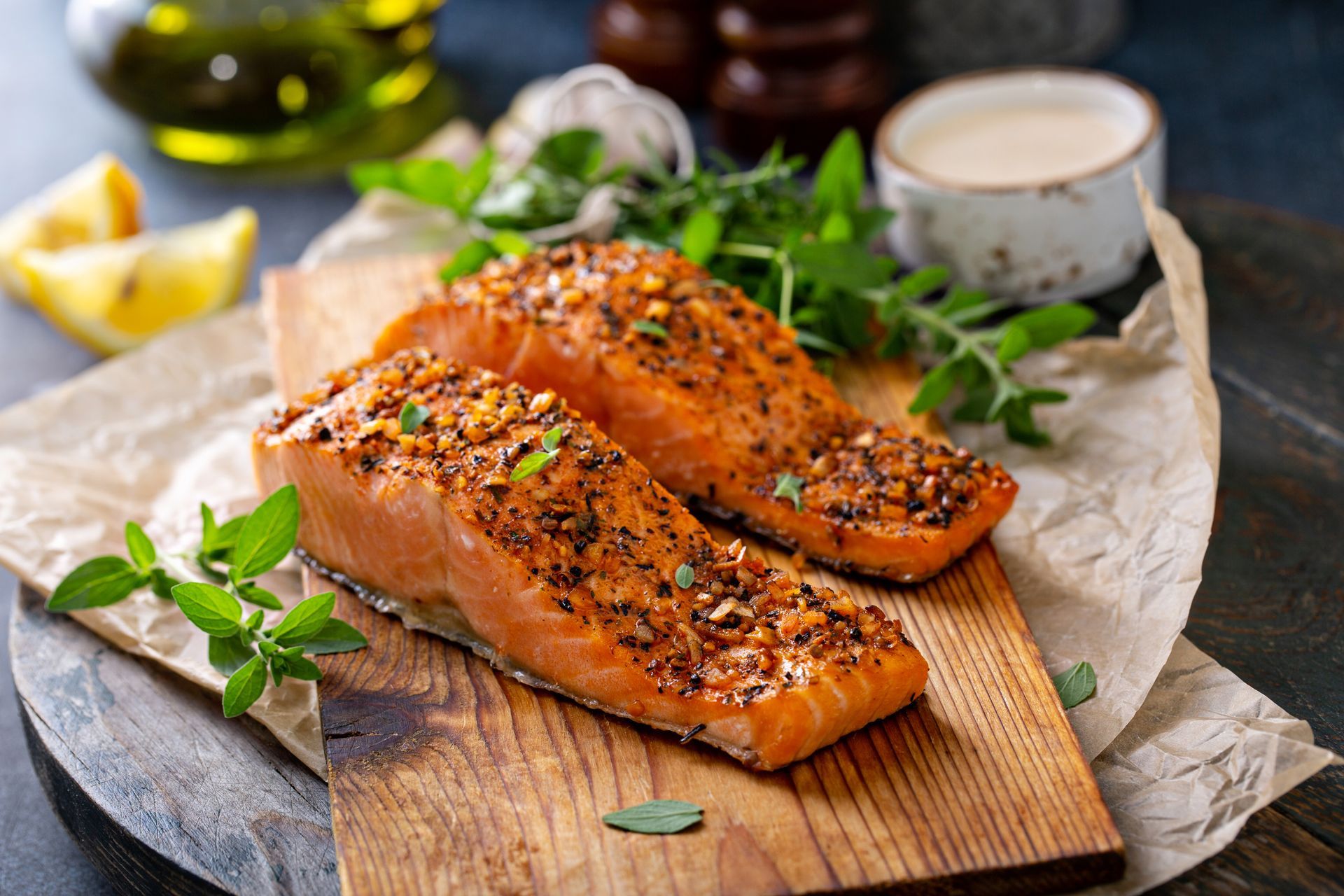 Two seasoned salmon fillets on a wooden board, with fresh herbs and sauce, close-up.