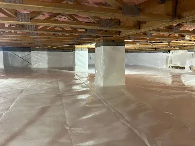 Crawlspace with vapor barrier and wrapped support posts. Wood beams and insulation are visible overhead.