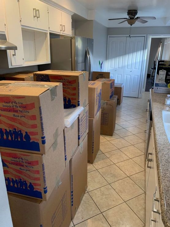 Kitchen with several moving boxes stacked along the tile floor. Cabinets and appliances visible.