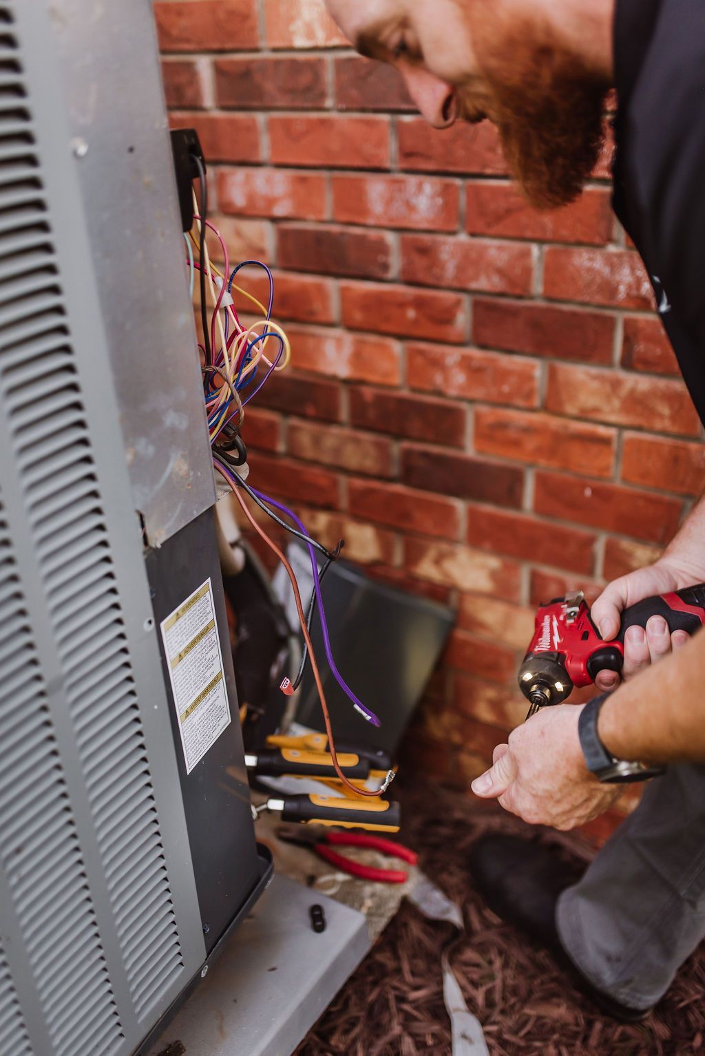 Tool bag with screwdrivers on an air conditioning unit in front of a house.