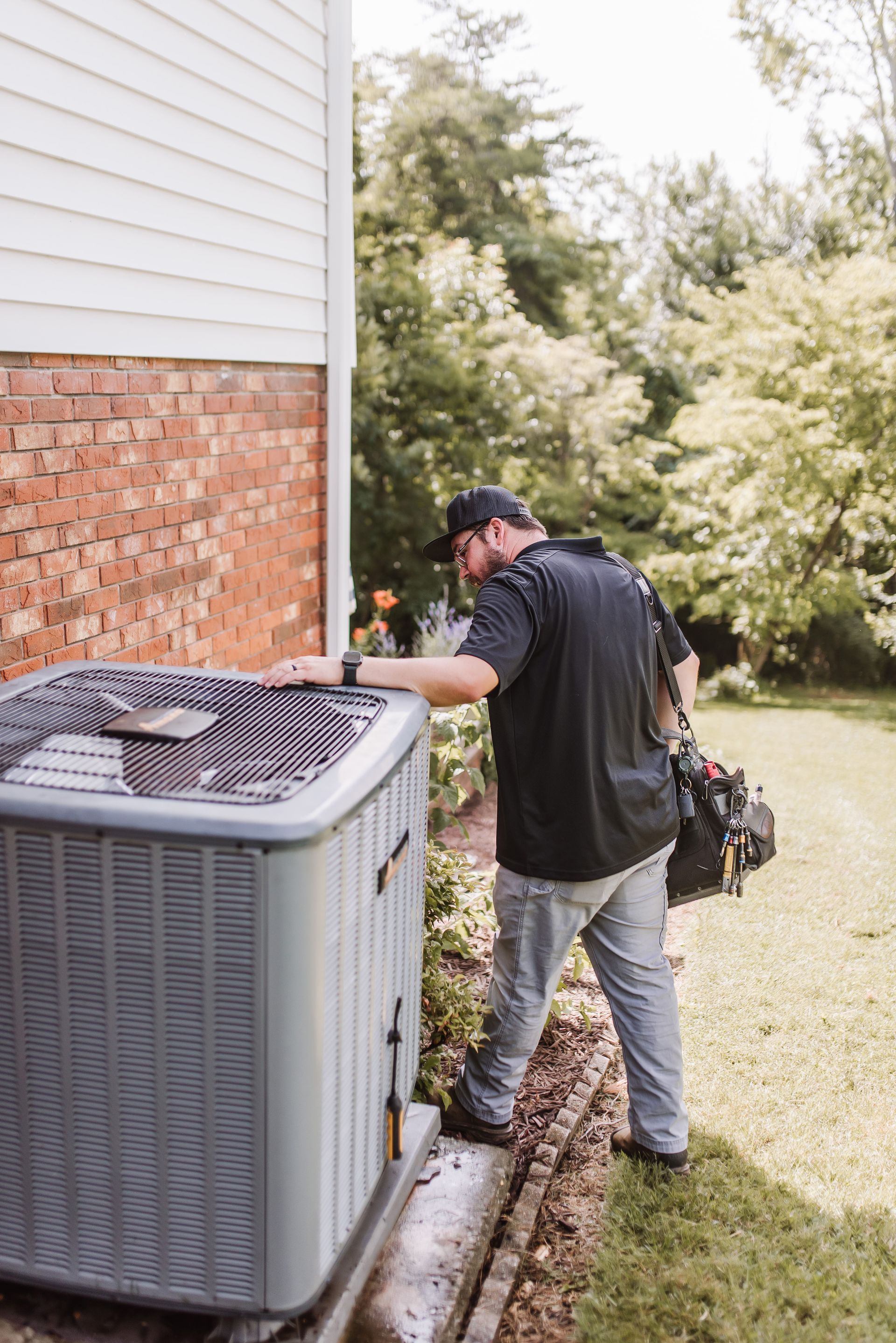 Tool bag with screwdrivers on an air conditioning unit in front of a house.