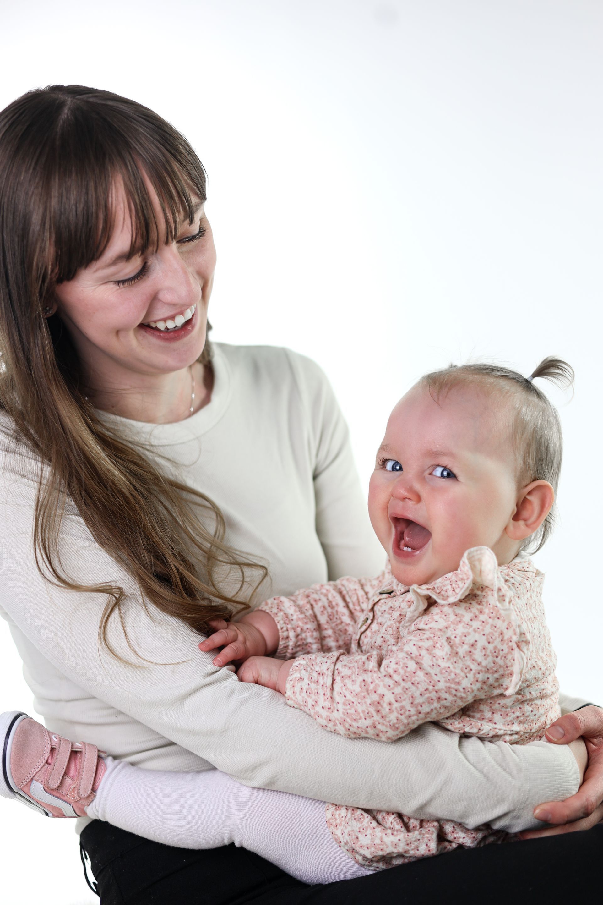 Vrouw met een lachende baby tegen een witte achtergrond. Ouder-kind fotografie.