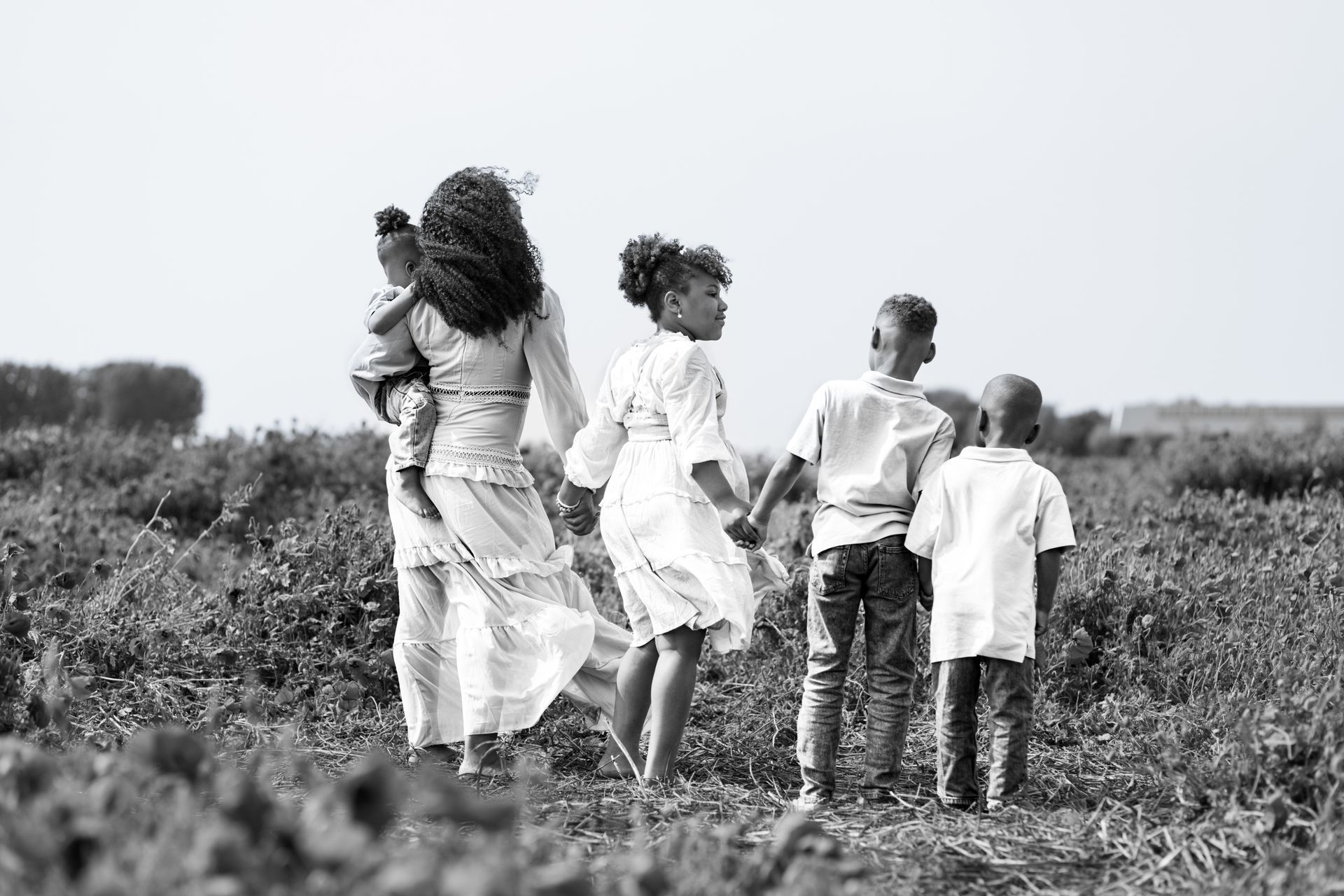 Vier kinderen lopen hand in hand door een grasveld, met hun rug naar de camera. Familiefotograaf