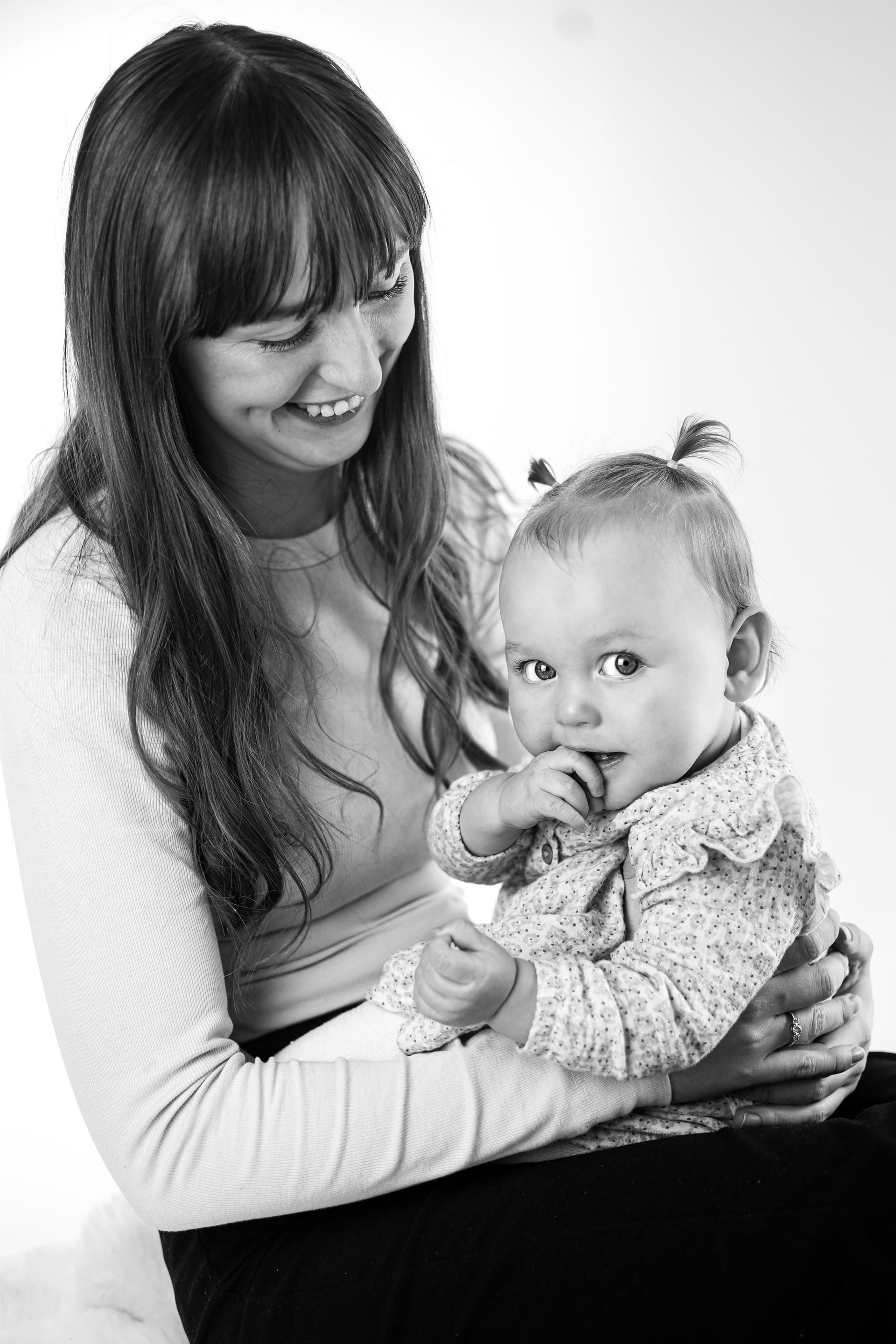 Vrouw die een baby vasthoudt en naar hen lacht in een zwart-witportret. Moeder-dochter fotoshoot.