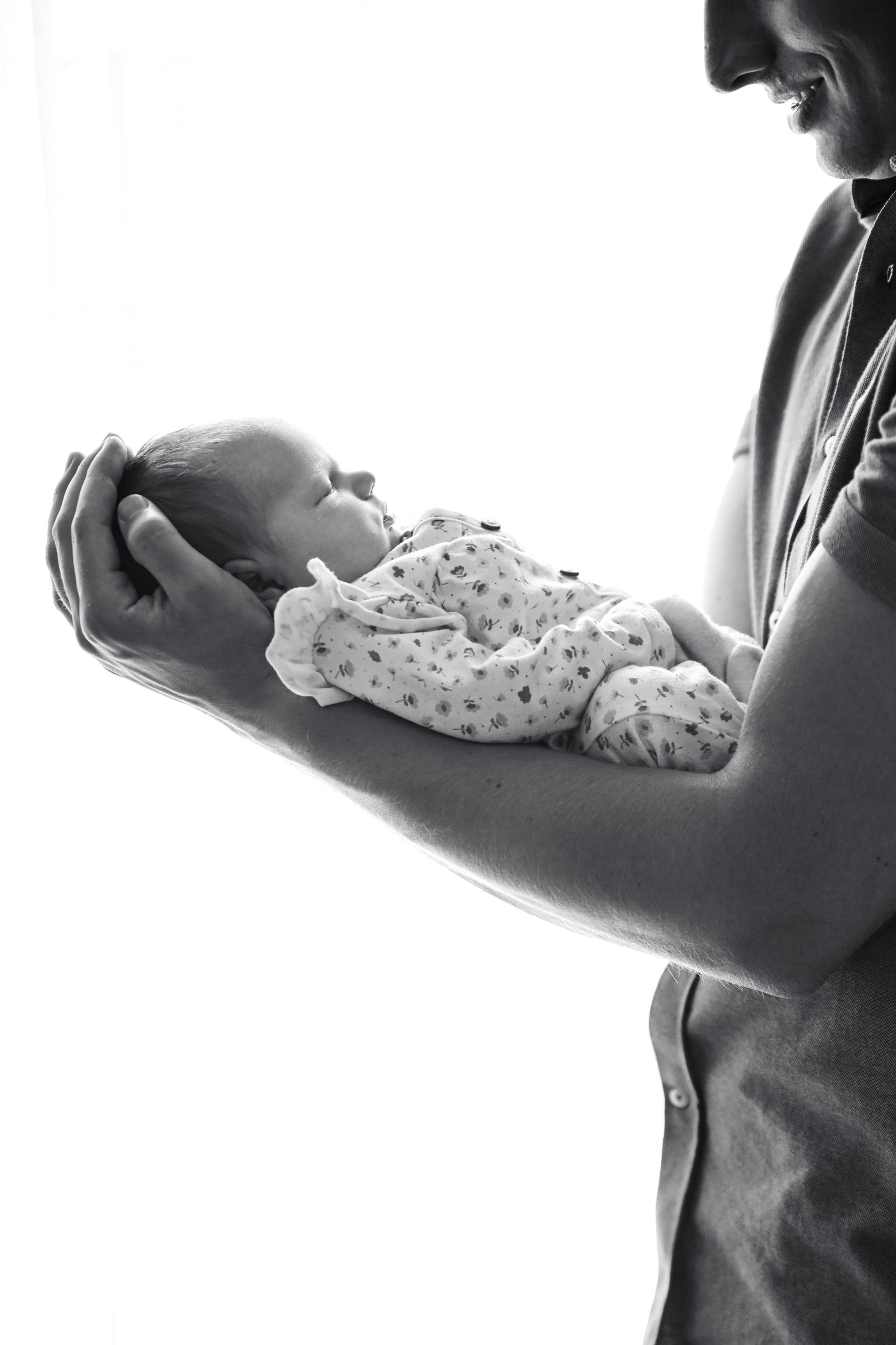 Een volwassene die een pasgeboren baby in beide handen vasthoudt, weergegeven in een zwart-wit silhouet. Newborn fotograaf.