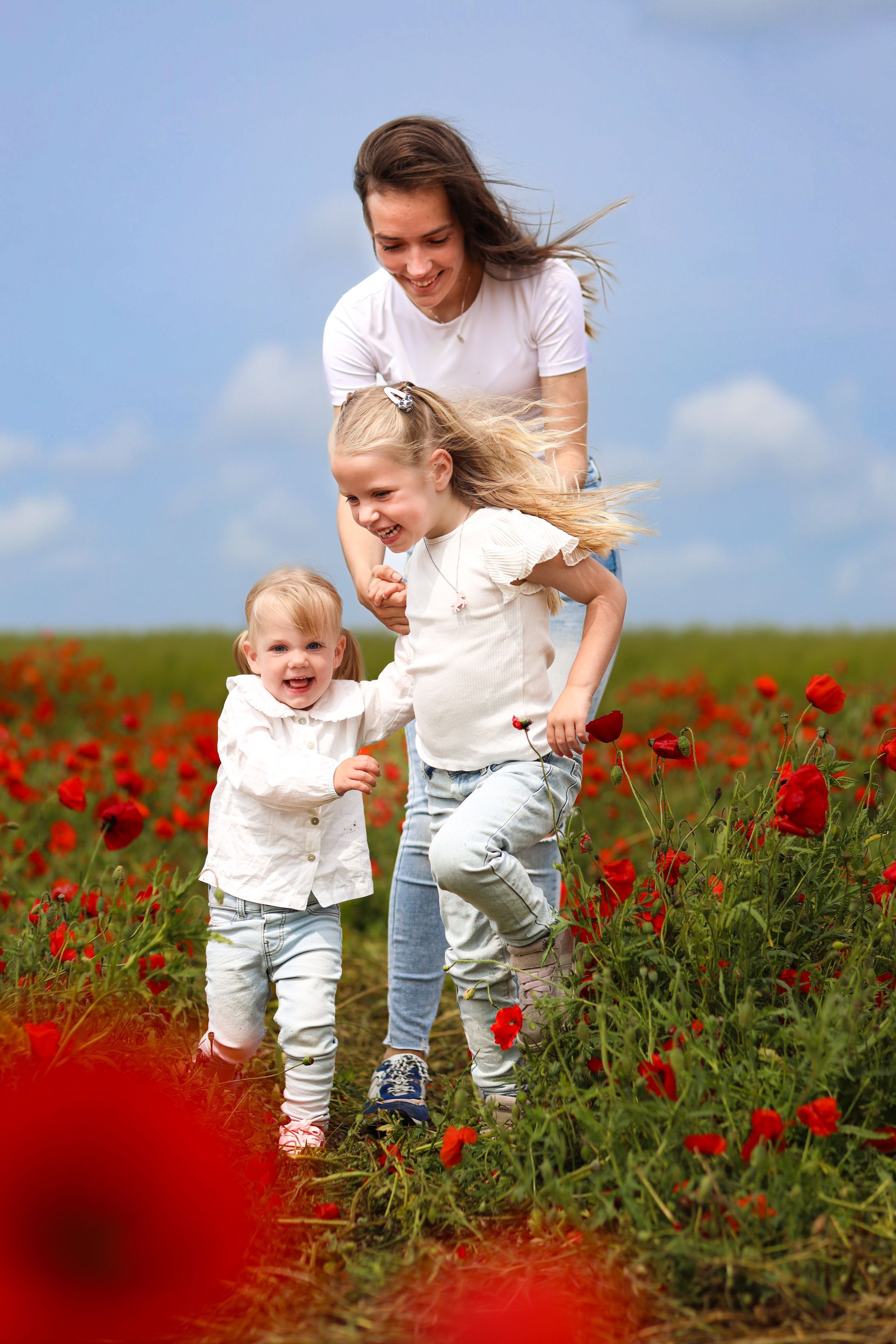 Vrouw en twee kinderen glimlachen in een veld vol rode klaprozen onder een blauwe hemel. Moeder met dochters. Fotoshoot.