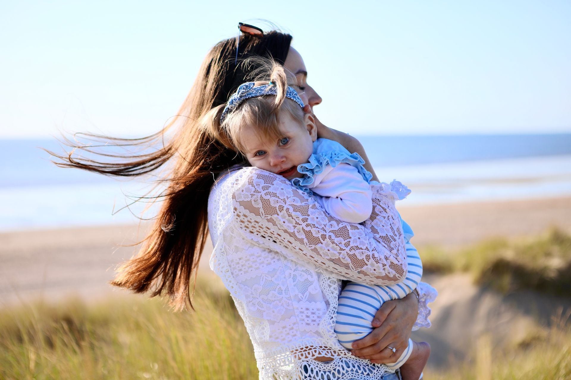 Een vrouw omhelst een kind op een winderig strand vlakbij de oceaan. Kinderfotografie.