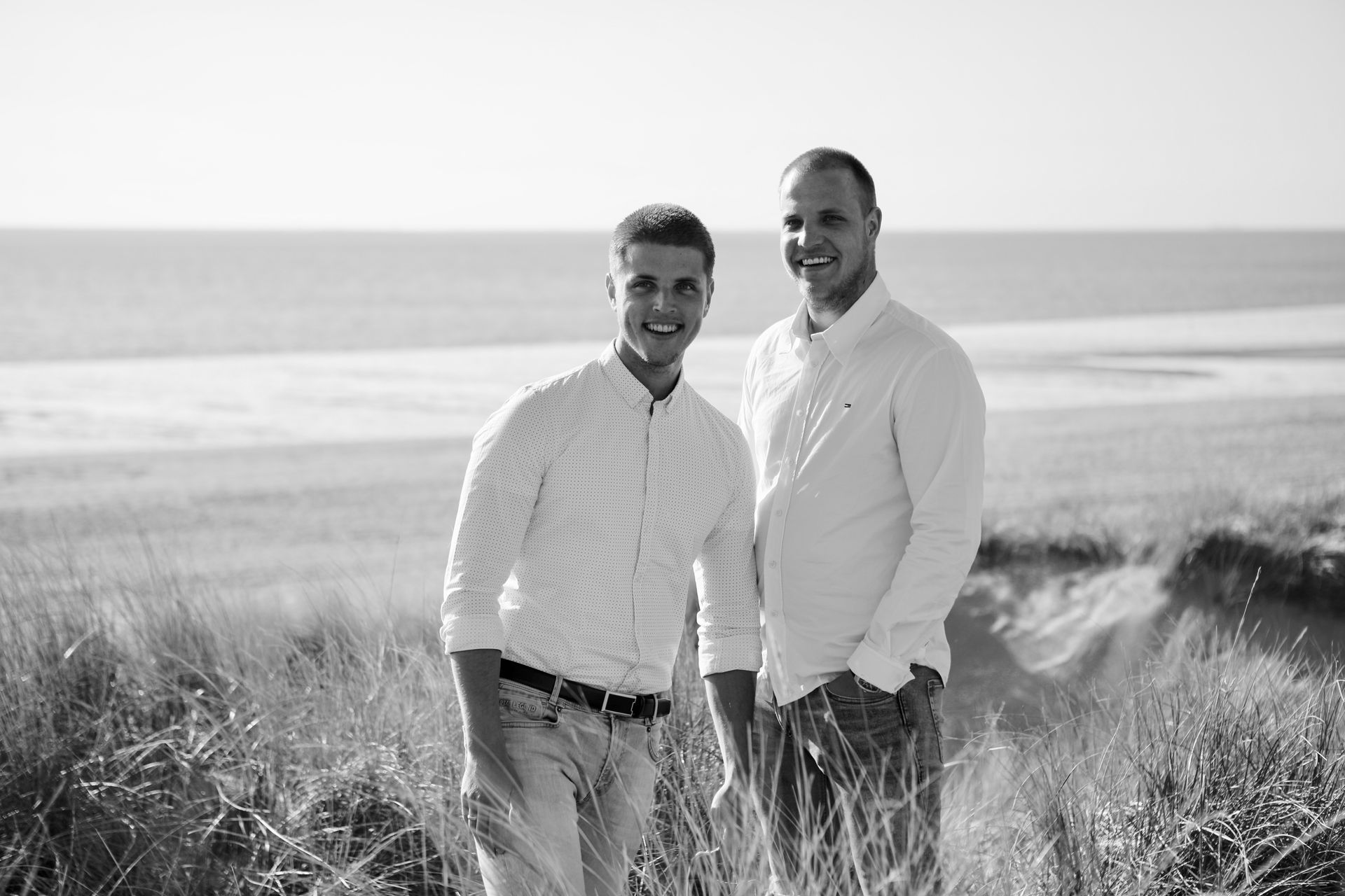 Twee mensen staan in een grasveld met de oceaan op de achtergrond. Familiefoto.
