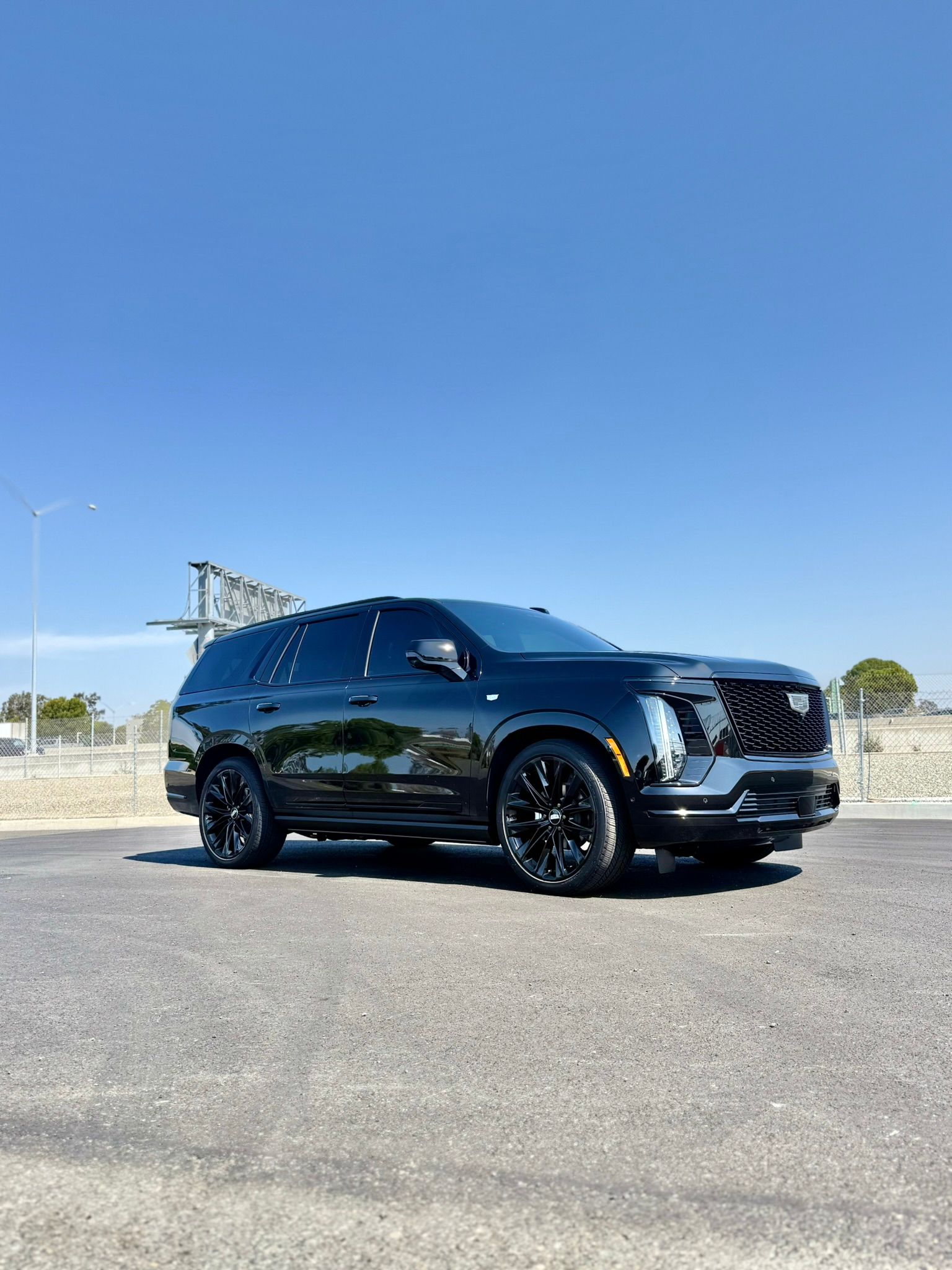 Black Cadillac with a shiny ceramic coating, parked on a smooth road under a clear blue sky.