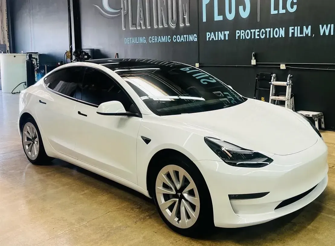 A white tesla model 3 is parked in a garage.