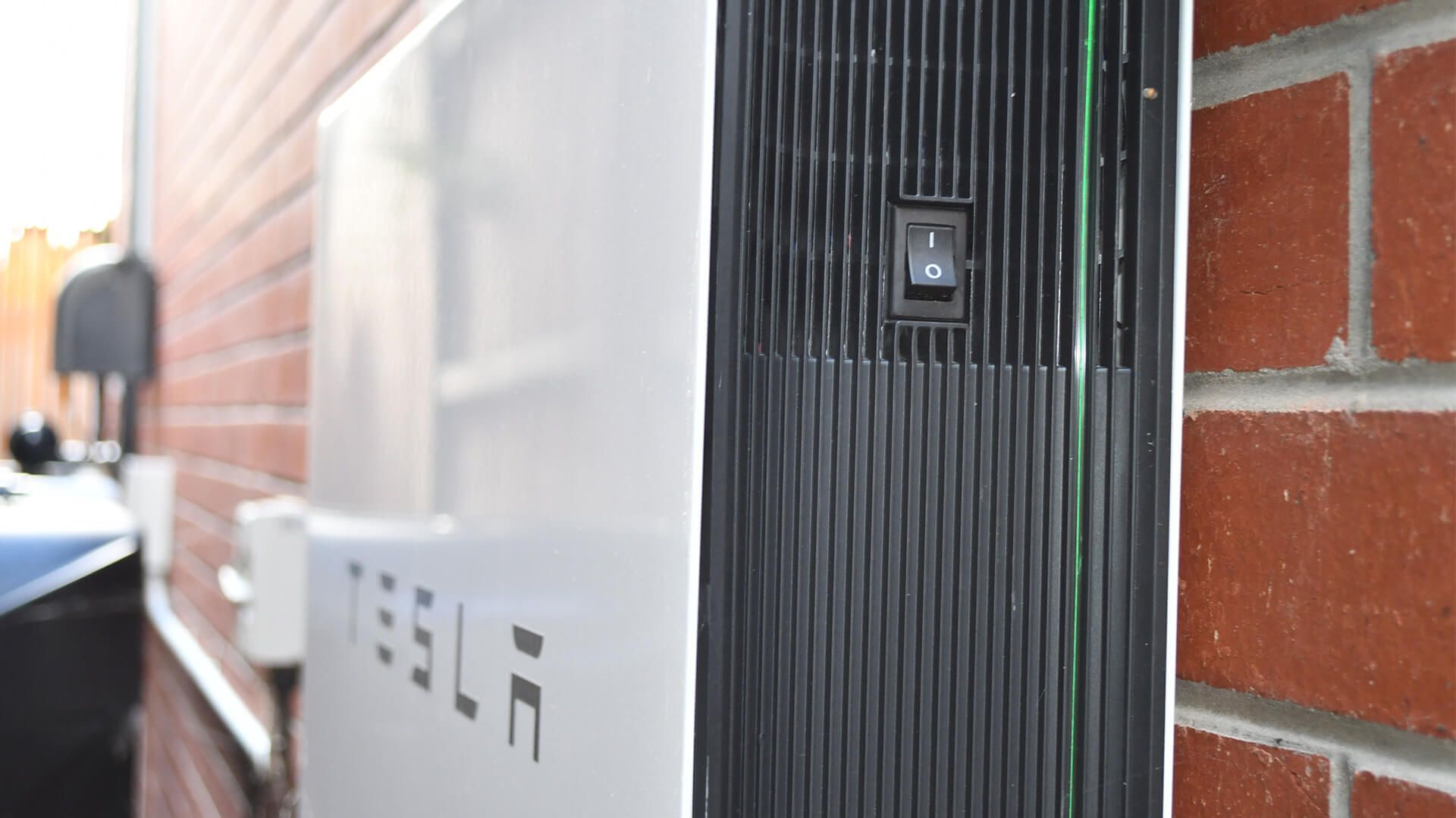 A tesla household battery is attached to a brick wall.