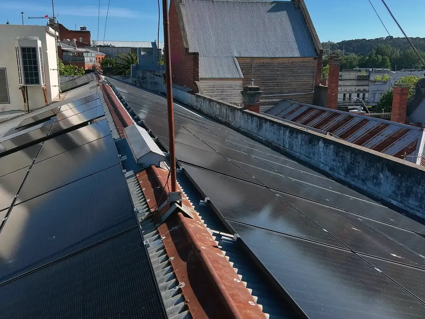 Solar panels on a building rooftop, with red metal, and other rooftops in the background.