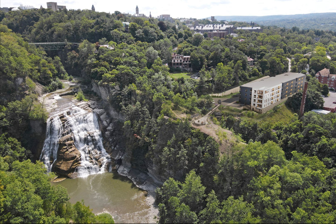 Waterfall cascading into a pool surrounded by lush green trees. A building sits nearby, overlooking the falls.