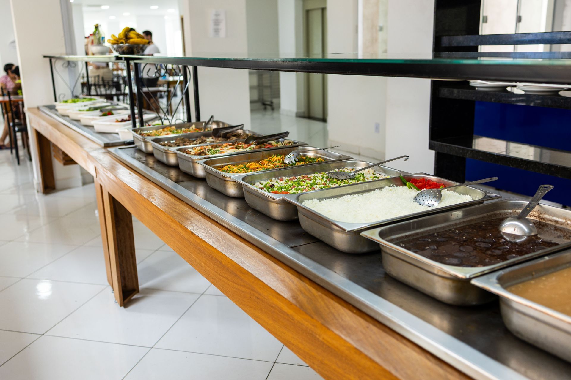 Mesa de buffet com diversas opções de comida em recipientes de aço inoxidável.