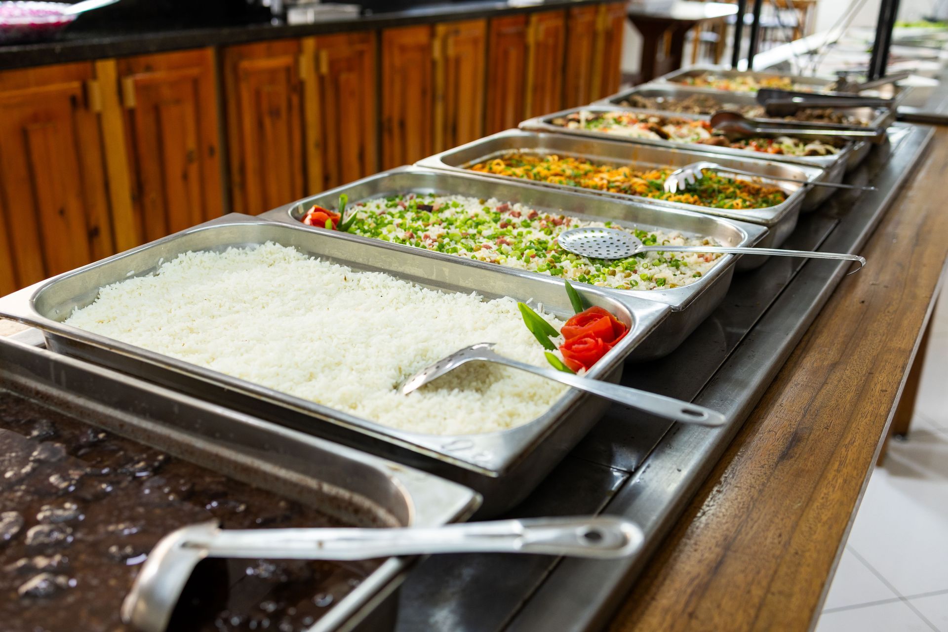 Buffet com diversas bandejas de comida, incluindo arroz, legumes e outros pratos.