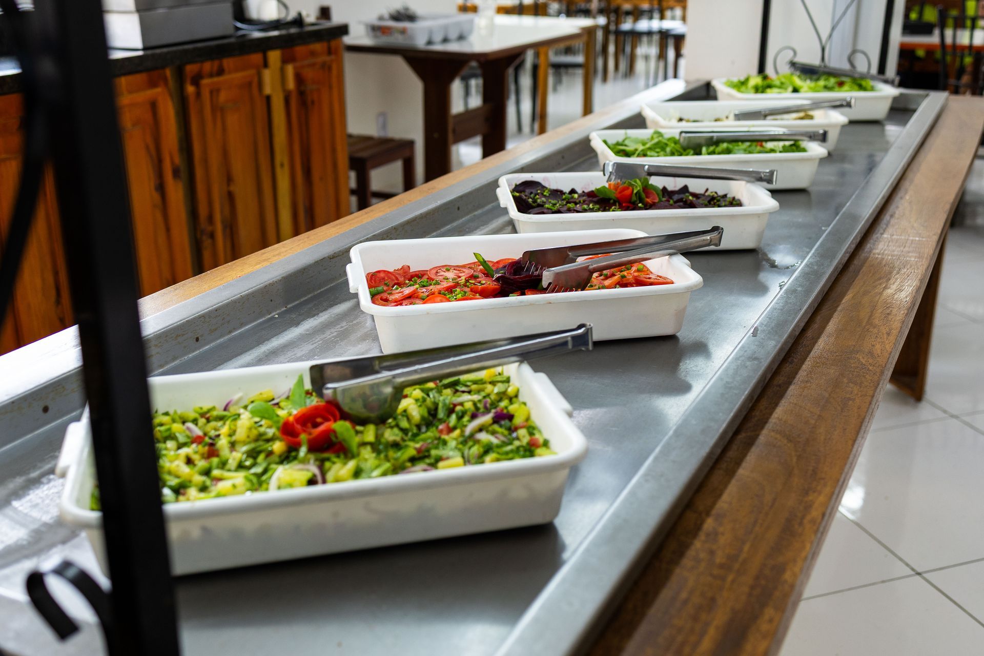 Bar de saladas com diversos pratos de vegetais coloridos em recipientes brancos.