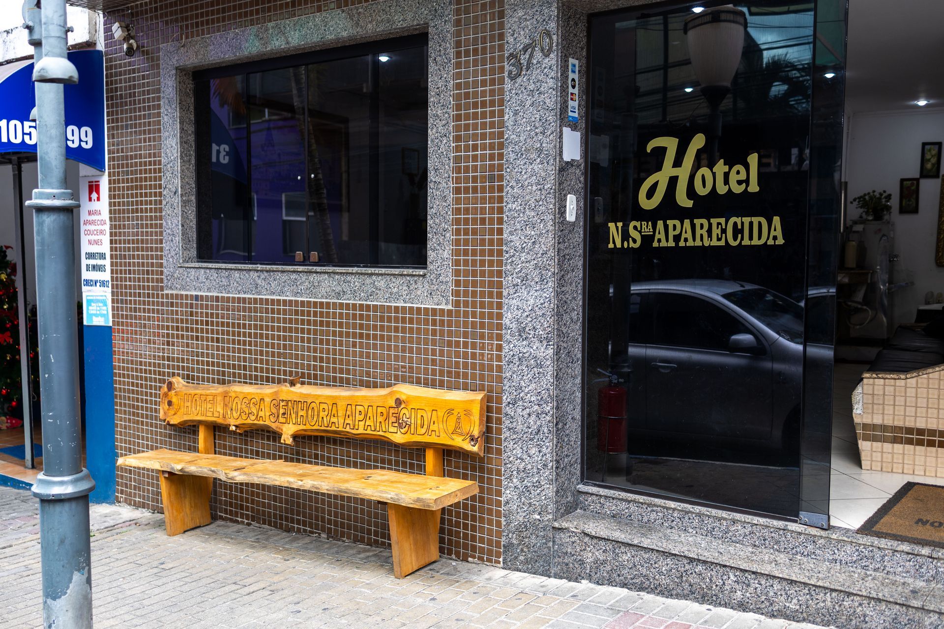 Entrada do Hotel NS Aparecida com um banco de madeira na calçada.
