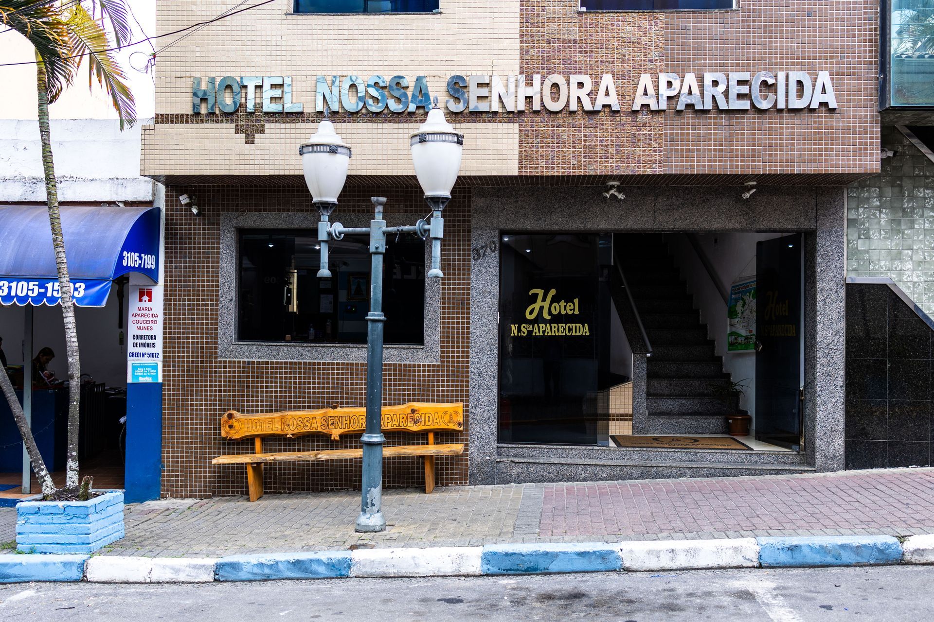 Hotel Nossa Senhora Aparecida exterior with a bench, street lamp, and entrance.