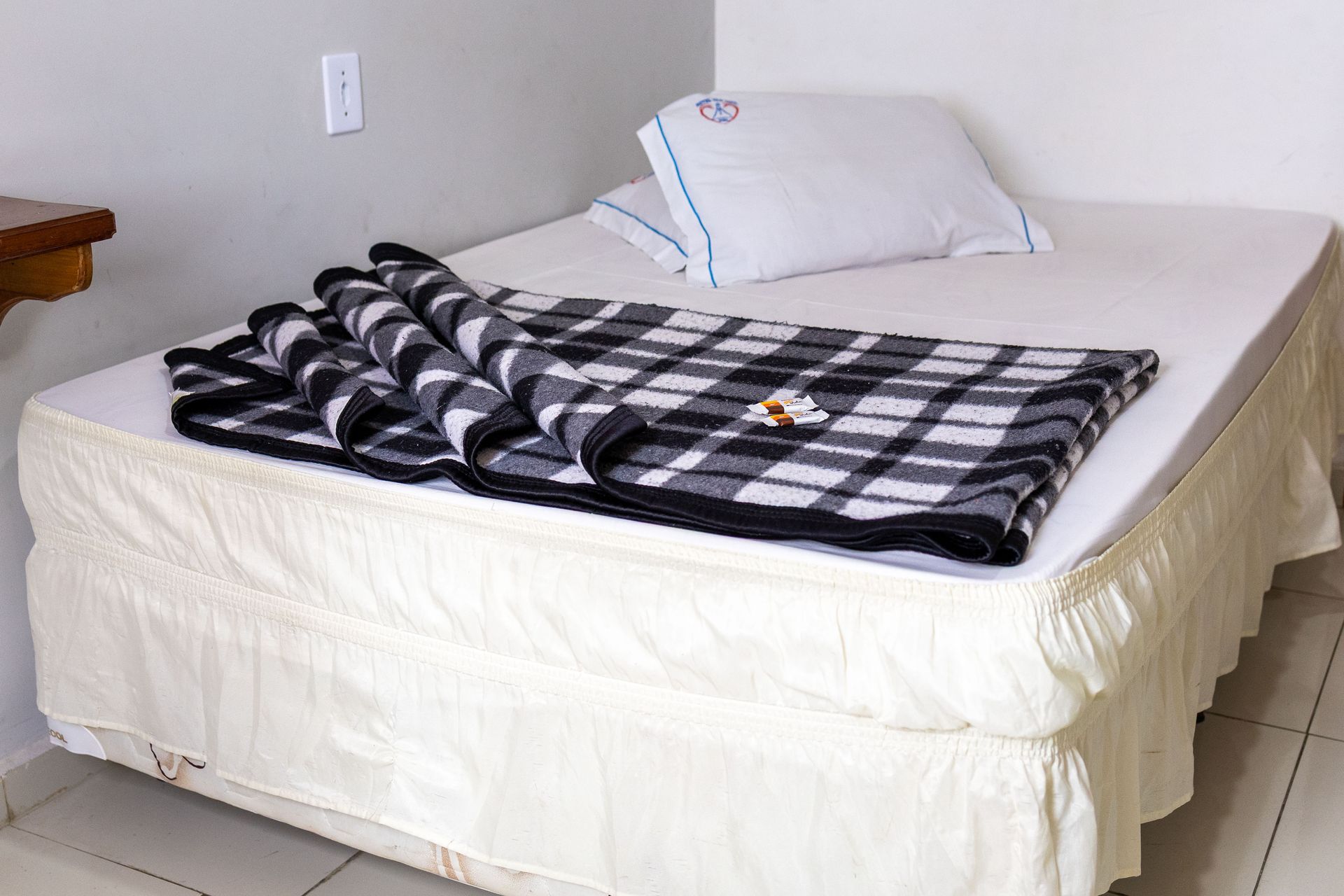 Cama com colchão branco, travesseiro e cobertor xadrez preto e cinza.