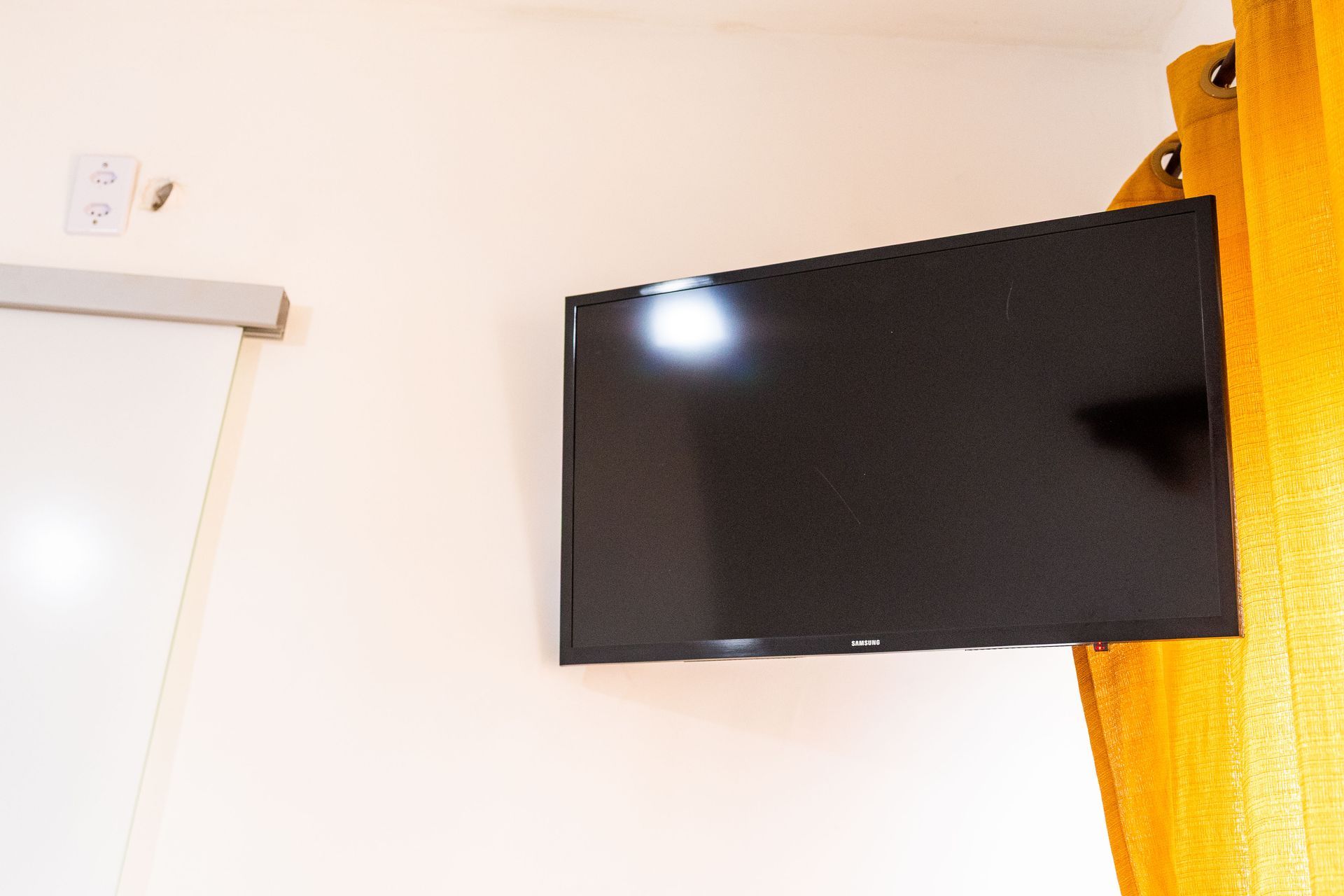 Televisor de tela plana montado em uma parede amarelo-clara, ao lado de cortinas amarelas.