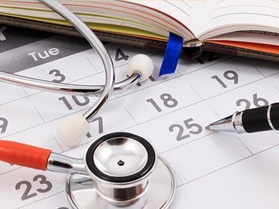 A stethoscope and a pen rest on a calendar page, symbolizing a medical appointment or health schedule.