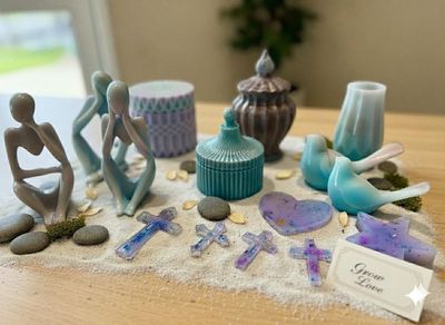 Blue and lavender sea glass sculptures, stones, and shells arranged on a sandy beach tray