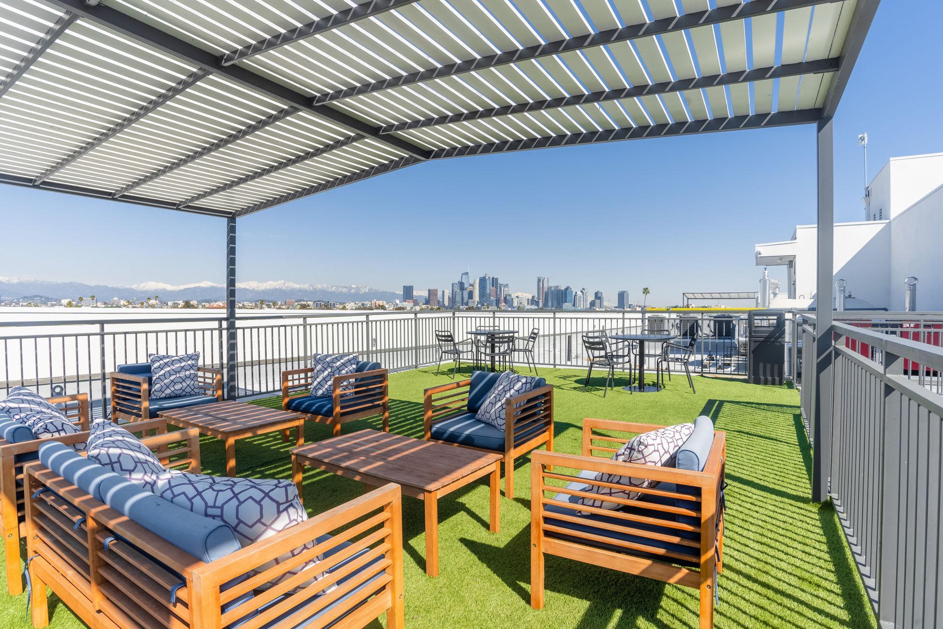 A rooftop patio with a pergola , chairs , tables and a view of the city.
