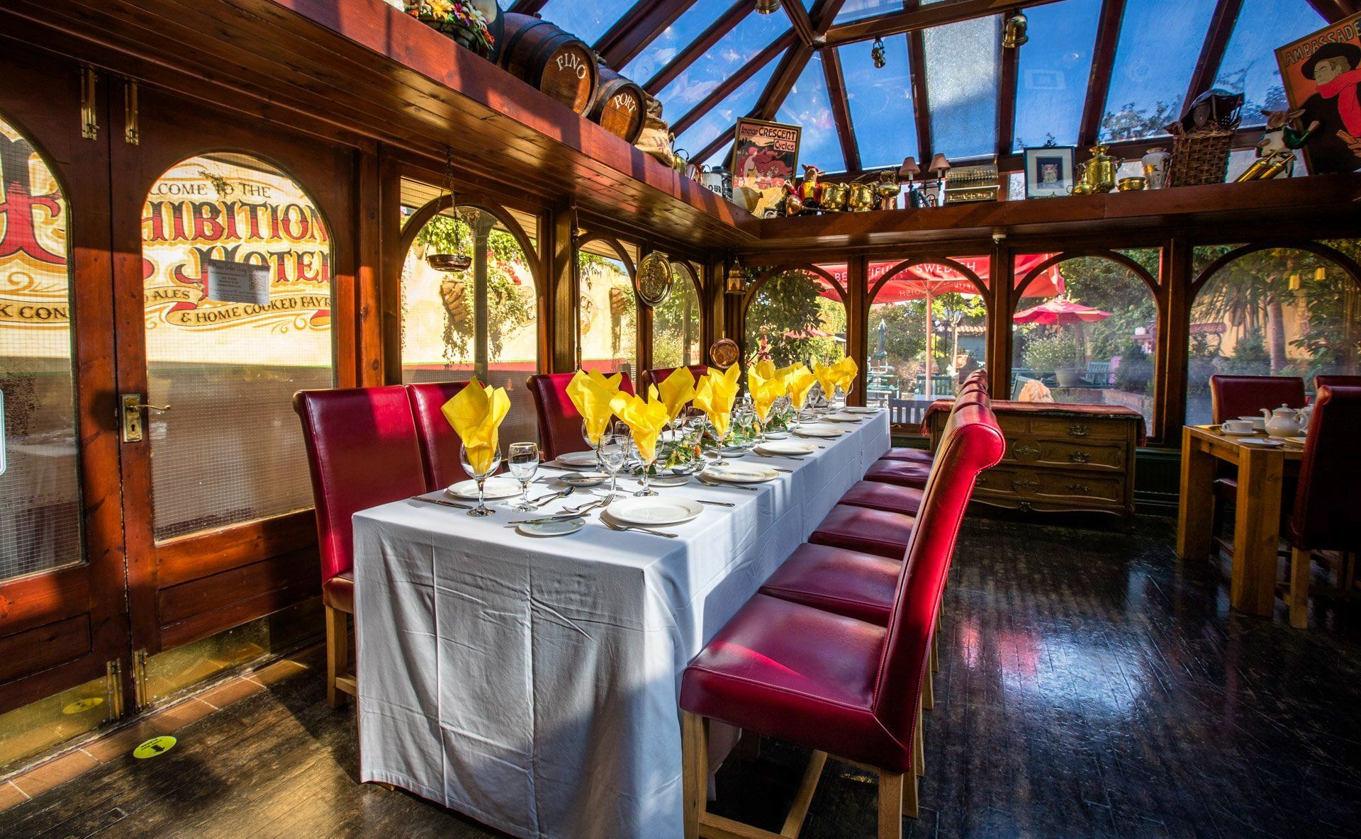 Long dining table set for a meal in a sunroom with red chairs and yellow napkins.
