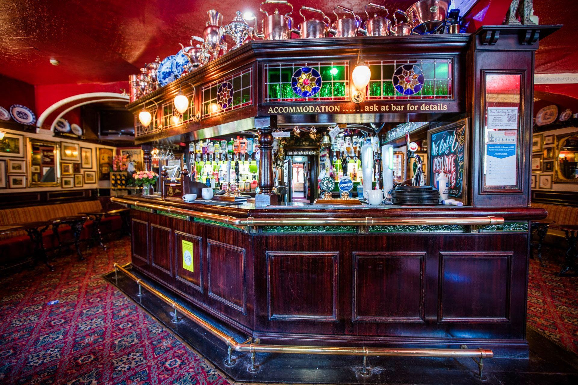 A richly decorated bar with dark wood, stained glass, and shelves of bottles.