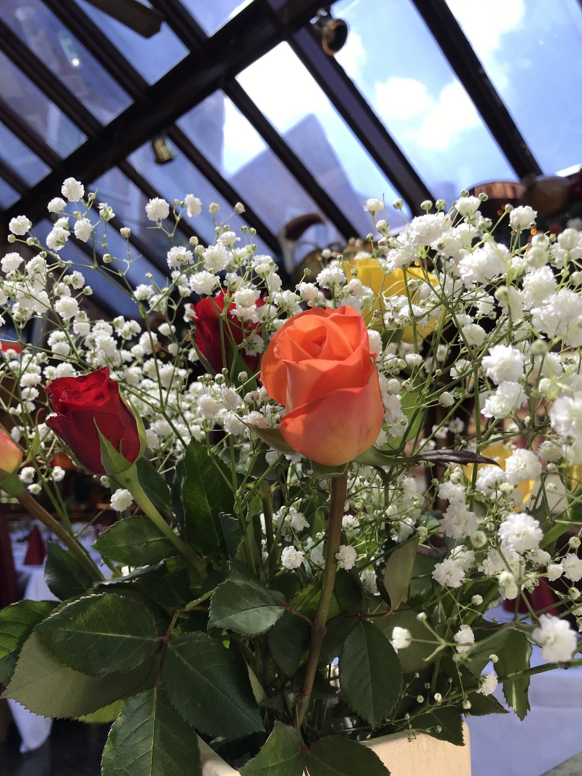 Orange rose in a bouquet of white baby's breath and other colored roses, under a glass ceiling.