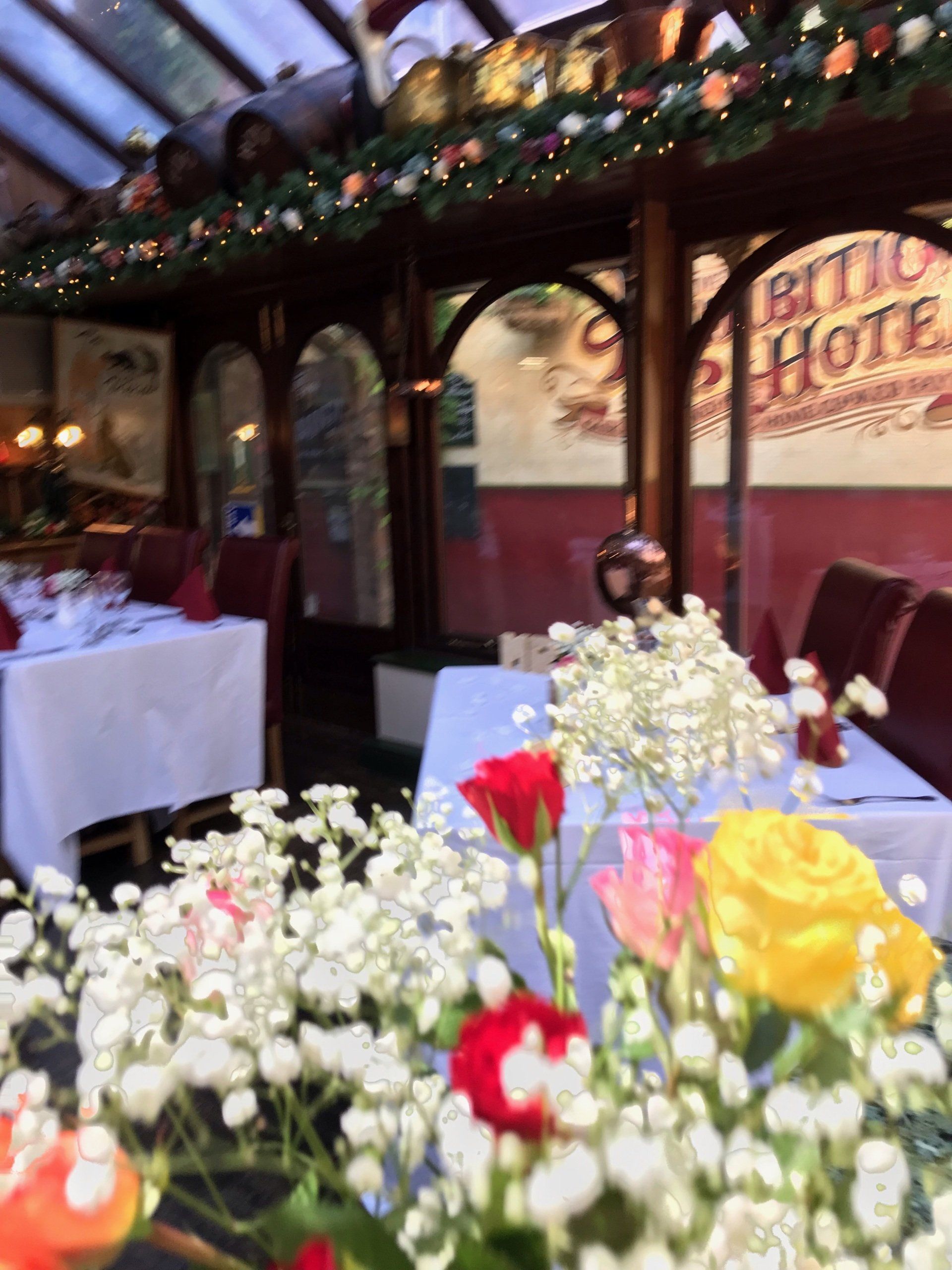 Restaurant interior, tables set with white cloths, red chairs, floral arrangements, blurred background, old-style sign.